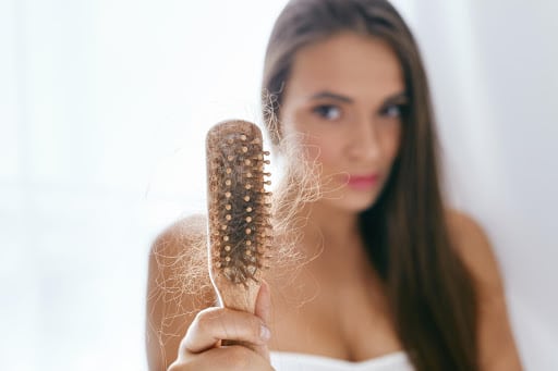Mulher segurando uma escova de cabelo com diversos fios